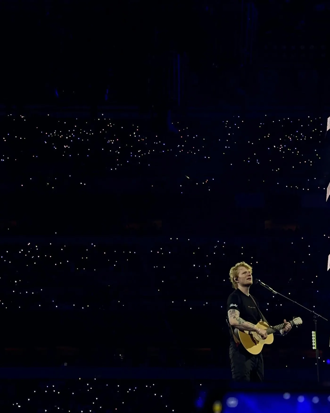 A stadium lit by phone lights while Ed Sheeran performs
